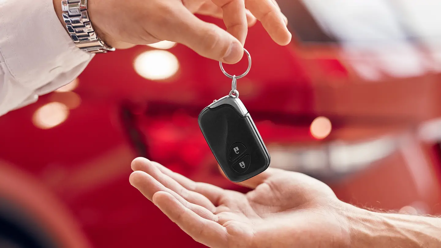 Autoverkäufer übergibt Fahrzeugschlüssel beim Autoverkauf