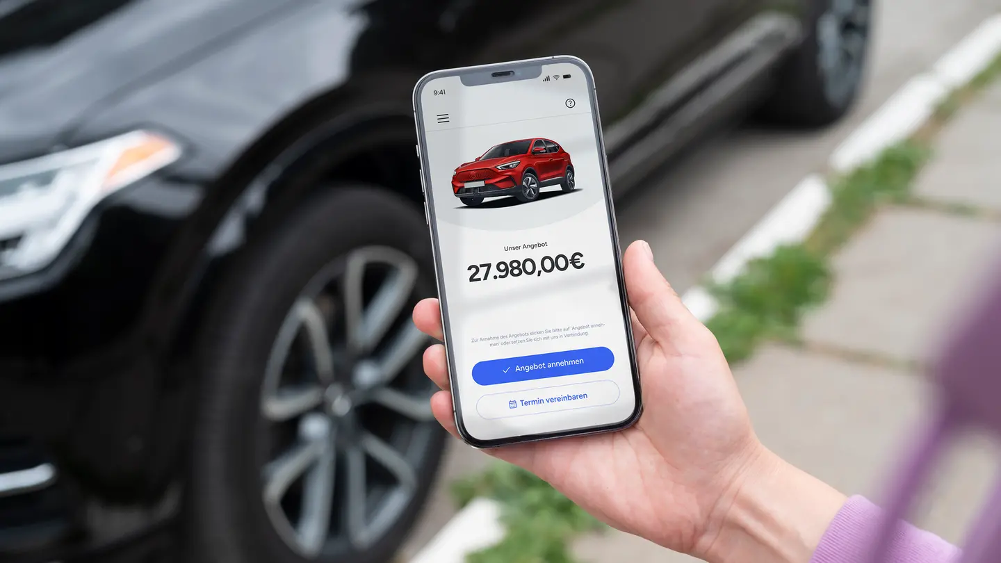 Mann vor Auto schauf auf Handy mit Kaufangebot auf Bildschirm